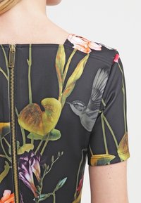 Robe imprimée florale avec un fond noir, des manches courtes et une fermeture éclair au dos. Le design comprend des fleurs colorées et une illustration d'oiseau.