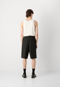 Musta, polvipituinen shortsit joustavalla vyötärökaitaleella, kaksi takataskua ja sileä pinta, yhdistettynä valkoiseen toppiin ja mustiin sukkiin.