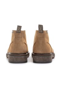 Botas de tobillo de ante marrón con punta redondeada, suela de goma texturizada y lengüetas en la parte trasera. Un simple bordado acentúa el diseño.