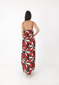 Robe maxi avec un fond noir, ornée de grands motifs floraux rouges et crème. Bretelles spaghetti ajustables et design cintré à la taille.