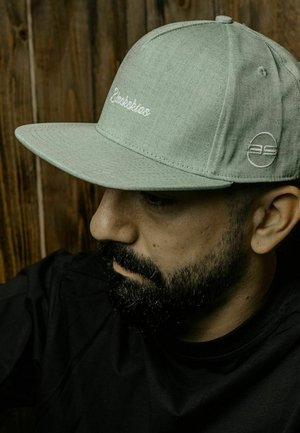 Green fabric cap with a flat brim. Features white embroidered logo and text. Simple design, minimal accents, smooth texture.