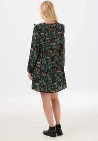Vestido de estampado floral con un fondo verde oscuro, que presenta patrones de animales coloridos, acentos de volantes en los hombros y una cintura ajustada.