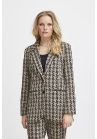 Blazer s vzorom houndstooth v béžovej a čiernej farbe, s výstrihom do písmena V, prednými vreckami a uzáverom na jeden gombík. Hladká textúra tkaniny.