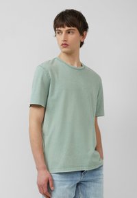 Bawełniany T-shirt w stonowanym odcieniu zieleni, z okrągłym dekoltem, krótkimi rękawami i luźnym krojem, w zestawieniu z jasnoniebieskimi dżinsami.