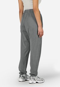 Γκρίζες φόρμες από μαλακό ύφασμα με ελαστική μέση, πλαϊνές τσέπες και στενές μανσέτες. Συνδυασμένες με γκρίζα αθλητικά παπούτσια.