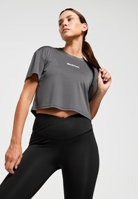 Grijs sportshirt met korte mouwen en cropped stijl, voorzien van een witte "Redmax" logo. Gecombineerd met hoge zwarte leggings. Glad textuur.