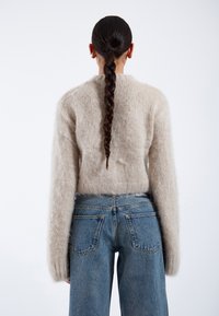 Beige fluffy sweater with long sleeves, paired with high-waisted blue denim jeans featuring a classic five-pocket design and visible seams.