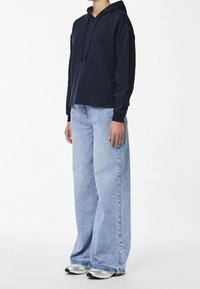 Marinblå hoodies med lös passform, ihop med ljusblå vida jeans och silverfärgade sneakers. Texturen verkar mjuk; materialen ser avslappnade ut.