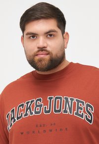 Barna, kereknyakú pulcsi merész fekete "JACK&JONES" logóval és fehér díszítéssel. Puha anyag, laza szabás, bordázott nyak.
