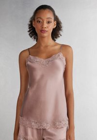 Satijnen camisole in zachtroze met kantafwerking langs de halslijn en zoom, voorzien van dunne verstelbare spaghettibandjes en een gladde textuur.
