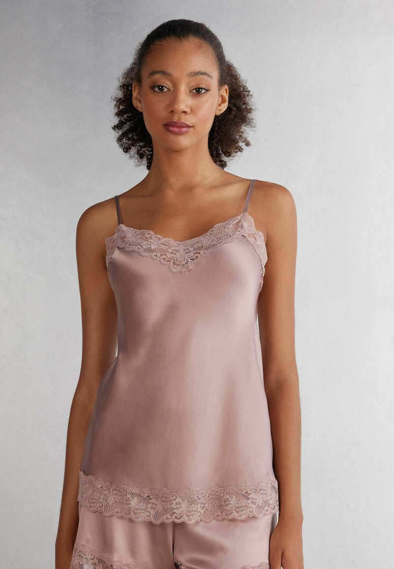 Satijnen camisole in zachtroze met kantafwerking langs de halslijn en zoom, voorzien van dunne verstelbare spaghettibandjes en een gladde textuur.
