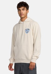 Beige hoodie van zacht materiaal, met een voorkantzak en een grafische logo in blauw en zwart met palmbomen. Relaxte pasvorm met trekkoorden.