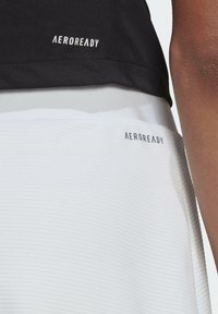 Top deportivo con una sección superior negra y una sección inferior blanca texturizada; presenta la marca "AEROREADY" en colores contrastantes.