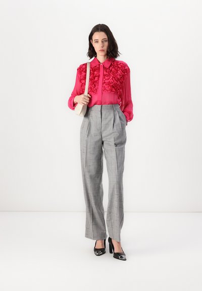 Blouse rose en voile avec des appliqués de roses en 3D, assortie à un pantalon à carreaux gris taille haute. Des escarpins en vernis noir complètent la tenue.