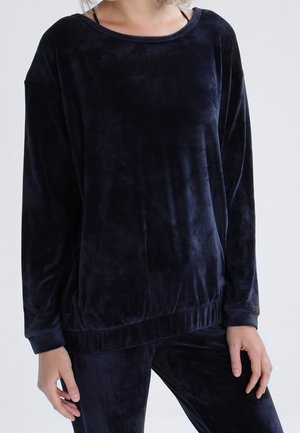 Woman wearing a dark navy velvet long-sleeve top and matching pants, standing with hands relaxed by sides.