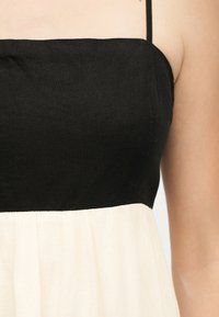 Γυναίκα που φοράει αμάνικο φόρεμα με μαύρο στενό κορσέ και φαρδιά, πλισέ λευκή φούστα, ορατή από τους ώμους έως τη μέση.