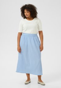 Light blue textured maxi skirt with elastic waistband, paired with a white fitted top and beige slip-on shoes.