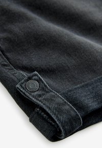 Mörkgrå denimtyg med en vikt fåll och en rund svart knappdetalj präglad med "NEXT DENIM." Slät textur och finmönster.