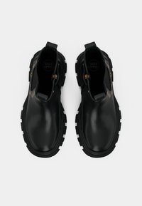 Botines negros de cuero con un acabado suave, suela negra gruesa, acentos de herrajes dorados y tiradores para facilitar su uso.