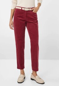 Pantalon en velours côtelé rouge à coupe droite, avec une ceinture blanche, des poches avant et des revers roulés. Associé à des mocassins beige.
