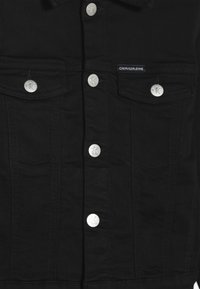 Schwarze Jeansjacke mit silbernen Knöpfen, zwei Brusttaschen und einem kleinen Markenetikett. Glatte Textur, klassisches Design.