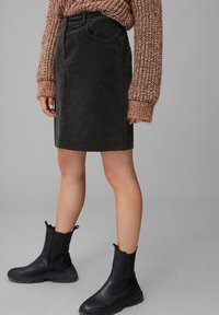 Jupe en velours côtelé noir à coupe droite, associée à un pull en tricot marron texturé et des bottines noires à semelle épaisse.