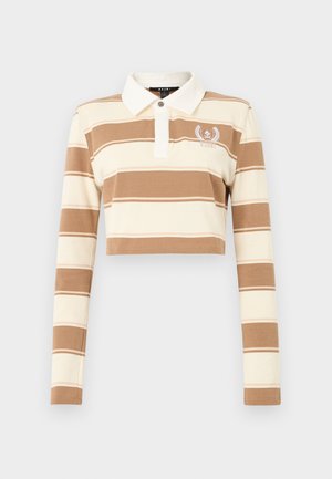 Joven mujer con polo de manga larga de rayas beige y marrón recortado, minifalda de cuadros, tacones negros de tiras, sosteniendo un pequeño bolso taupe.