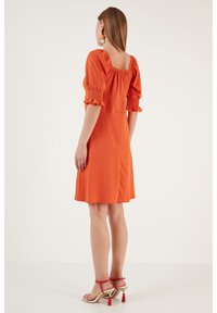 Orange short dress with puff sleeves and a square neckline, featuring textured fabric and a flared skirt, paired with multi-colored heels.