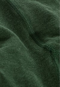 Tissu tricoté vert foncé avec une texture douce, présentant une surface lisse et des motifs de couture visibles le long des bords.