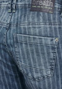 Vaqueros de mezclilla en azul descolorido con rayas verticales, con un bolsillo trasero y una etiqueta oscura que dice "breath" y "Cecil".