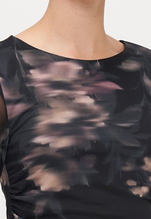 Close-up van een torso die een doorschijnende zwarte top draagt met abstracte paarse en beige bloemmotieven en een ronde halslijn.