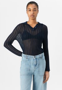 Blusa navy trasparente a maniche lunghe con un motivo testurizzato e colletto. Abbinata a jeans azzurri a vita alta con un taglio classico.