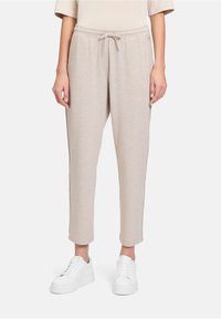 Lichtbeige sweatpants met een elastische tailleband en trekkoord. Glad textuur, taps toelopende pijpen en zijzakken. Draag ze met witte sneakers.