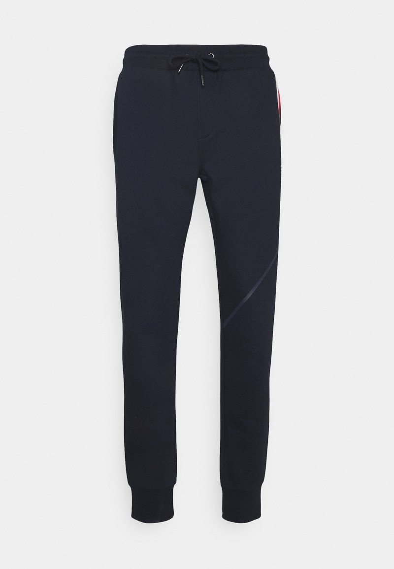 Marineblå sweatpants lavet af blødt stof, med elastisk talje og snøre, ribbede manchetter og en subtil design detalje på siden.