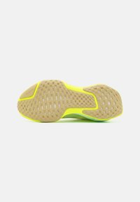 Semelle de chaussure beige clair avec un motif de grip texturé, comportant un accent jaune vif le long du bord et un détail du logo Nike moulé.