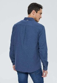 Chemise à manches longues à boutons de couleur bleu foncé, en tissu texturé, avec un design de patte de dos et des poignets à boutons.