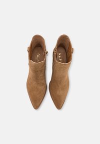 Pari ruskeasta mokasta valmistettuja nilkkakenkiä kärjelle osoittavalla varrella ja sivuvetoketjuilla, nähtynä ylhäältä valkoista taustaa vasten.