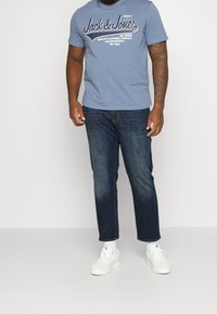 Camiseta de algodón de color azul claro con texto en blanco, combinada con pantalones vaqueros oscuros y zapatillas blancas. Conjunto simple y casual con líneas limpias.