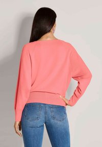 Koraalroze trui met een relaxed fit, geribde zoom en lange mouwen, gecombineerd met blauwe skinny jeans. Glad breiwerk, minimale details.