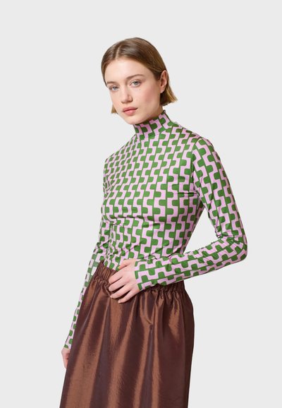 Langarm-Turtleneck-Oberteil im grün-rosa geometrischen Muster, aus elastischem Stoff gefertigt. Kombiniert mit einem braunen, glänzenden, gerafften Rock.