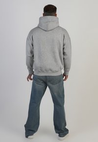 Grauer Hoodie mit großer Kapuze und gerippten Bündchen, kombiniert mit hellblauen, weiten Jeans. Einfaches Design, keine sichtbaren Muster oder Grafiken.