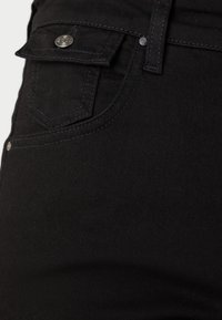 Jean en denim noir avec une vue rapprochée de la poche avant, présentant un petit bouton et des détails de couture subtils sur le tissu.