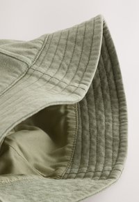 Cappello a secchiello verde chiaro con esterno texturizzato e trapuntato e fodera interna liscia. Presenta una tesa ampia e flessibile.