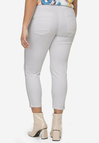 Hvide ankellange jeans med en glat tekstur, har to baglommer og en sidelagskæring detalje. Kombineret med beige blokhælede støvler.
