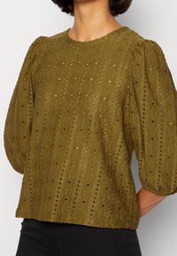 Maglione verde oliva con tessuto testurizzato, maniche a sbuffo e motivo a occhiello; presenta un collo tondo e una vestibilità ampia.