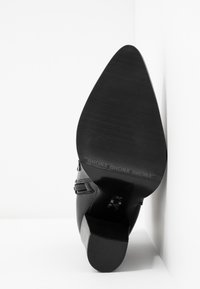 Botte noire élégante à bout pointu avec un talon bloc, semelle visible avec le logo "BRONX" et fermeture éclair latérale, présentée sur un fond blanc en coin.