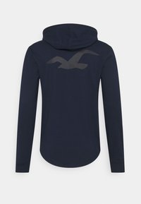 Marinblå långärmad hoodie tillverkad av mjukt tyg, med rundad nederkant och en stor grå mås-grafik på baksidan.