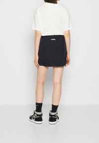 Svart kjol av lättviktigt material med elastisk midja, i kombination med en vit t-shirt och svarta högskor.