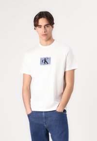 White cotton t-shirt featuring a graphic print in blue and black with "Calvin Klein" and "New York City" text. Crew neck design.