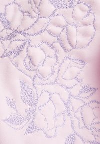 Ljust rosa tyg med intrikata lavendelblomsterbroderier och blad. Texturen är slät och framhäver upphöjda stygnmönster.